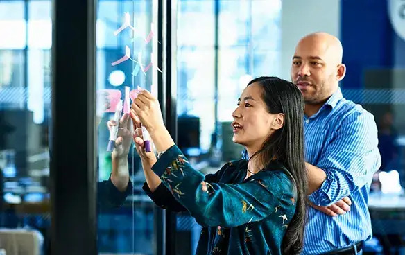 Two individuals collaborating as they write on a transparent glass wall, showcasing creativity and teamwork in action.