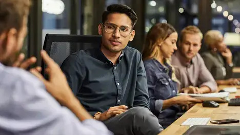 A diverse group of professionals engaged in discussion while seated around a conference table in an office setting.