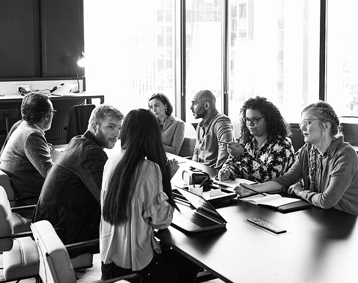 A diverse group of individuals engaged in discussion around a conference table in a professional meeting room.