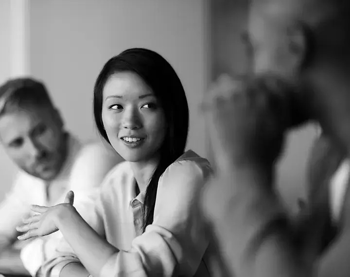 A black and white image depicting a group of individuals engaged in a meeting, showcasing collaboration and discussion.