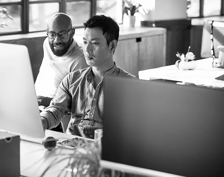 Two men collaborating on a computer in a modern office setting, focused on their work and sharing ideas.